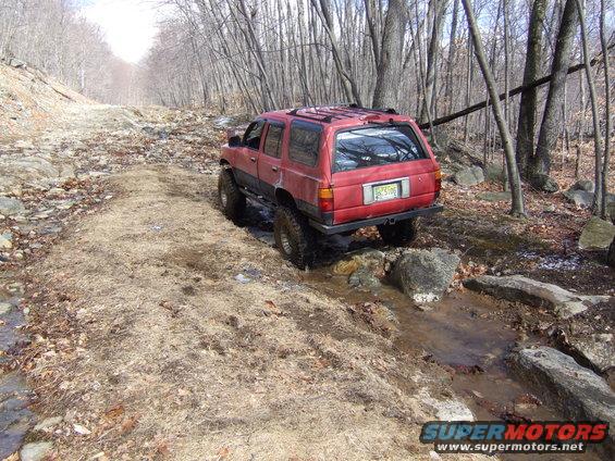 Red SUV with lifted suspension driving through a rocky, wet trail