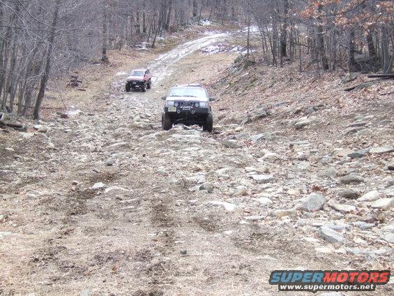 Two SUVs navigate a rocky, wooded trail