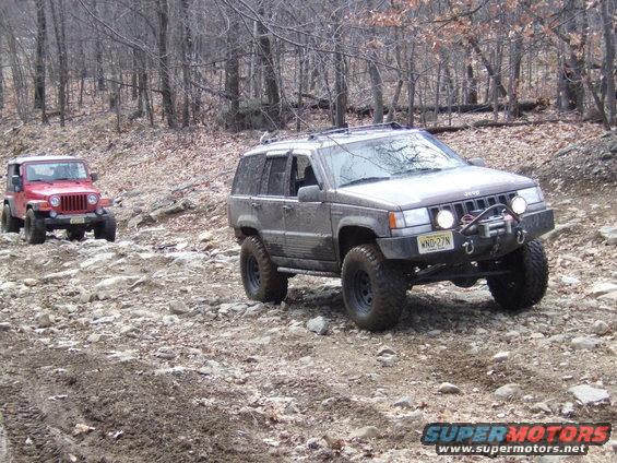 Gray Jeep Grand Cherokee with winch and red Jeep Wrangler on rocky trail in woods