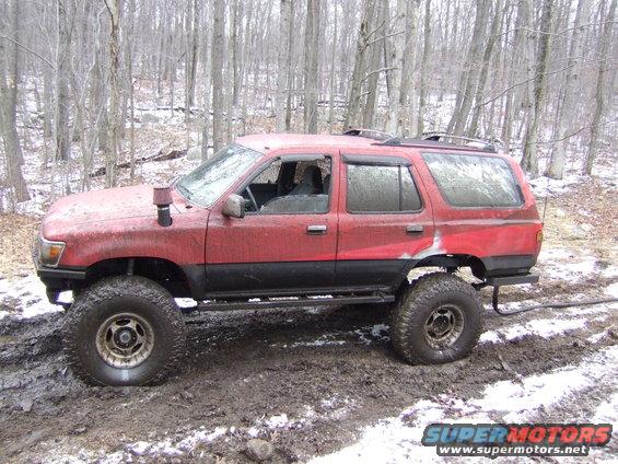 Red SUV with large tires and snorkel, stuck in mud with snow on the ground