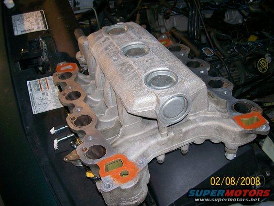 Engine intake manifold with gaskets removed, sitting on a dark surface. Date stamp reads 02/08/2008