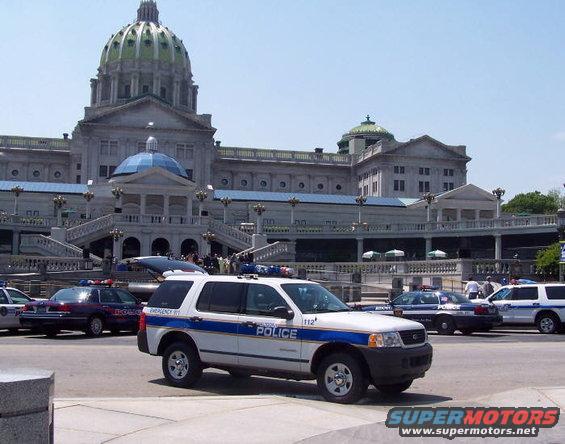 White police SUV with blue stripe and "POLICE" text in front of a government building