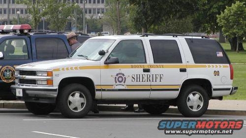 White Boone County Sheriff SUV parked next to a police SUV. Yellow stripe along the side