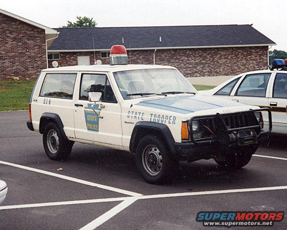 White Jeep Cherokee State Trooper with light bar and push bumper parked in a lot