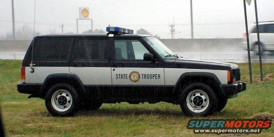 Side view of a black and silver Jeep Cherokee XJ with "STATE TROOPER" text and a light bar