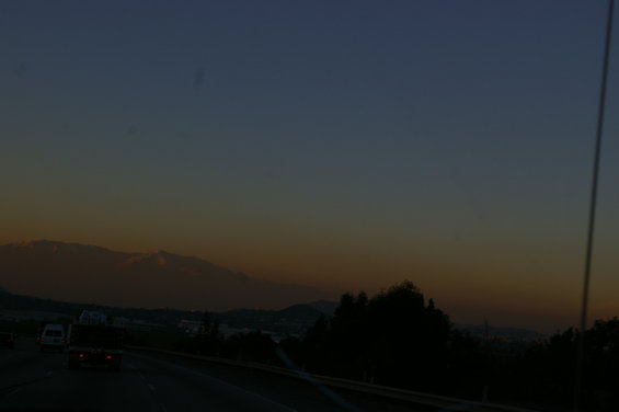 Highway driving at dusk with mountains in the distance and trees silhouetted