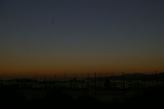 Sunset sky gradient over buildings and a fence line