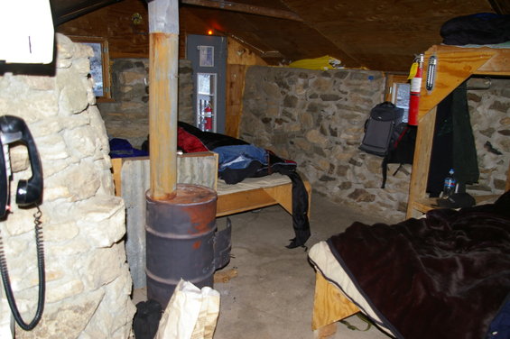 Interior of a rustic cabin with beds, a wood stove, and a telephone