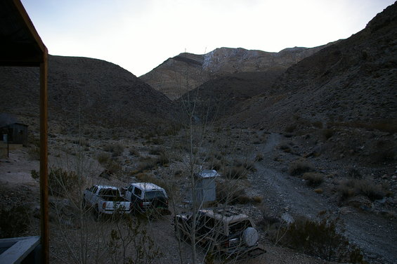 three old vehicles parked in a dry, rocky canyon with hills in the background