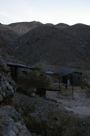 Desert scene with dilapidated metal buildings and rocky hills under a pale sky