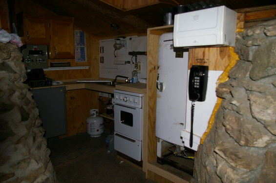 Interior of a rustic room with a propane tank, white stove, and black telephone mounted on a wall