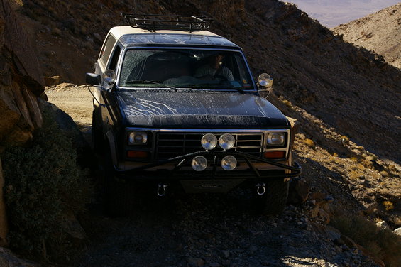 Ford Bronco driving on a dirt road in a canyon. It has a roof rack and extra lights on the front