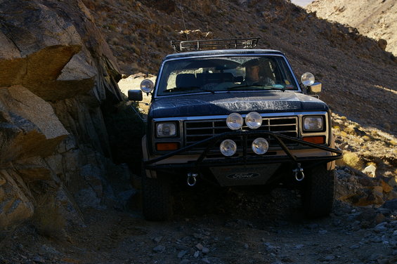 1986 Ford Bronco navigating a narrow, rocky off-road path with a driver visible
