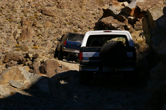 White Ford Bronco with spare tire on rear, driving on rocky terrain