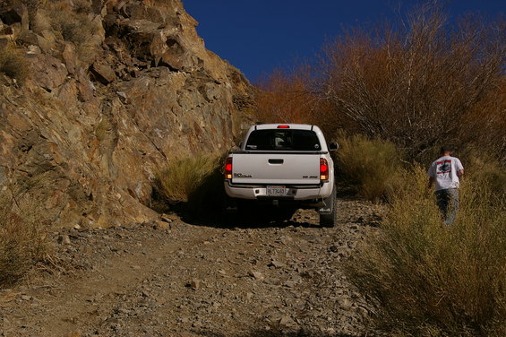 White Toyota Tacoma pickup truck on a rocky, off-road trail with a person walking away from the camera