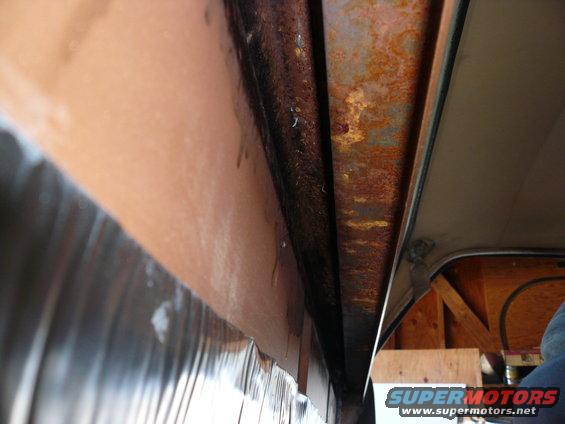 Close-up of rusted metal frame and brown interior paneling inside a vehicle
