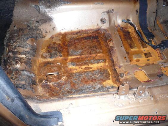 severely rusted floor pan inside a vehicle, showing metal fatigue and corrosion