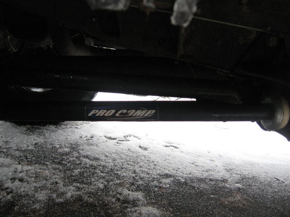 Pro Comp suspension part with white lettering on black background, mounted under a vehicle