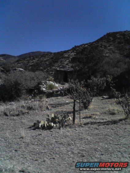Stone structure with a doorway sits in a dry, hilly landscape with sparse vegetation and cacti