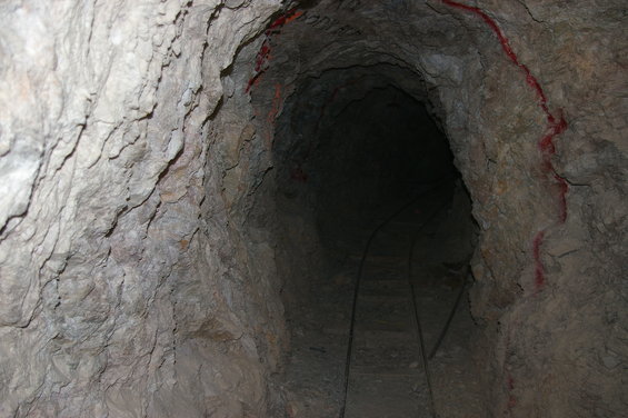 Mine tunnel interior with narrow gauge tracks disappearing into darkness. Red markings on the rock walls