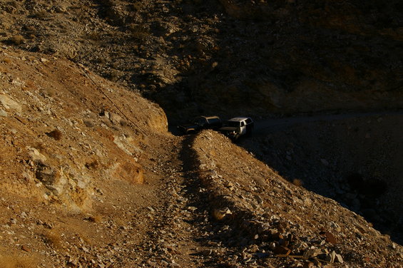 Two SUVs parked on a narrow dirt road winding through a rocky canyon