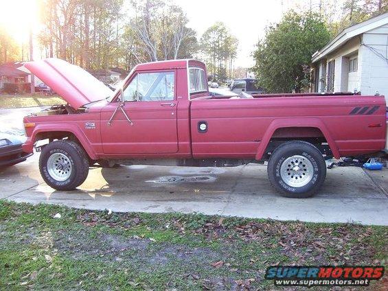 Red Jeep pickup truck, side view, hood open. Appears to be from the 1980s