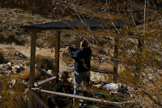 Two people at an outdoor shooting range, one aiming a handgun