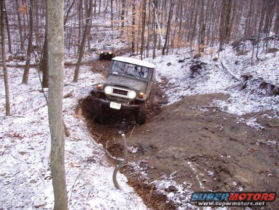 Toyota Land Cruiser FJ40 going off-road on a snowy, muddy trail with another vehicle behind it