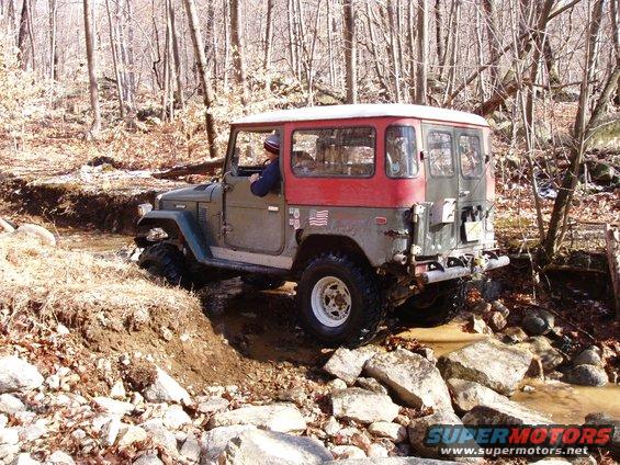 1976 Toyota Land Cruiser driving through a rocky stream in a wooded area