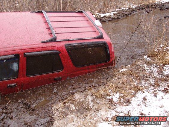 Red SUV stuck in muddy water, side view, roof rack visible