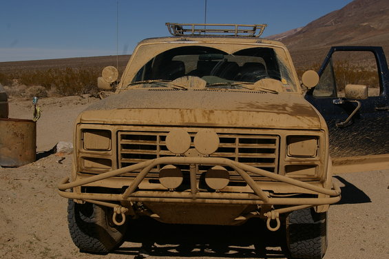 Dust-covered tan off-road vehicle front view with aftermarket bumper and roof rack