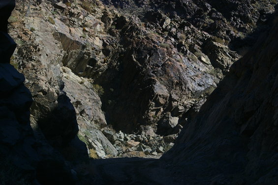 Dirt road goes through a narrow, rocky canyon with steep, sunlit cliffs