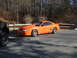 1995 Ford Mustang - An orange Ford Mustang is parked in an outdoor lot with trees in the background.