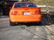 1995 Ford Mustang - The rear of an orange 1995 Ford Mustang GT is visible, parked next to a dark-colored SUV.