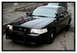 1998 Ford Crown Victoria - A black police car is parked outside next to another vehicle.