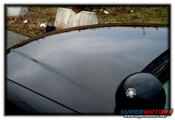 Black car hood and side mirror with reflection, concrete barriers in background