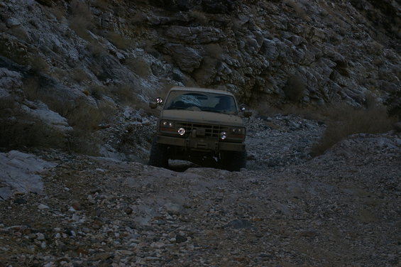 Tan 1986 Ford Bronco driving on a rocky trail, front view