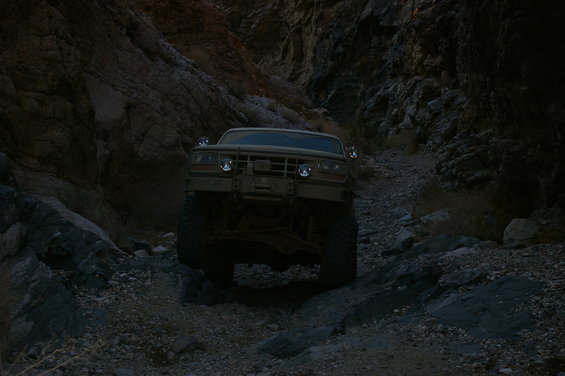 tan off-road vehicle with large tires driving on a rocky trail in a canyon