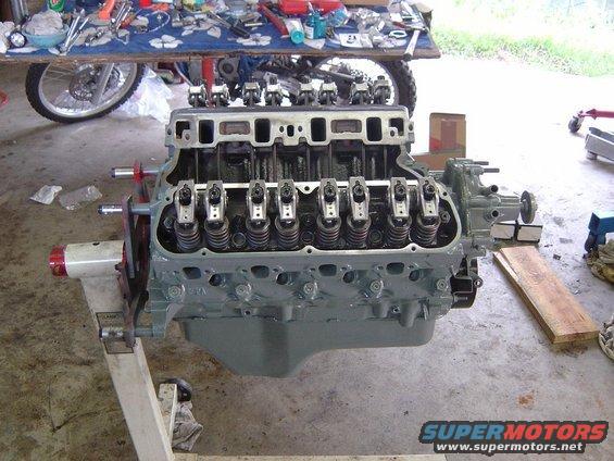 Gray V8 engine on a stand, with valve covers removed, showing rocker arms and springs