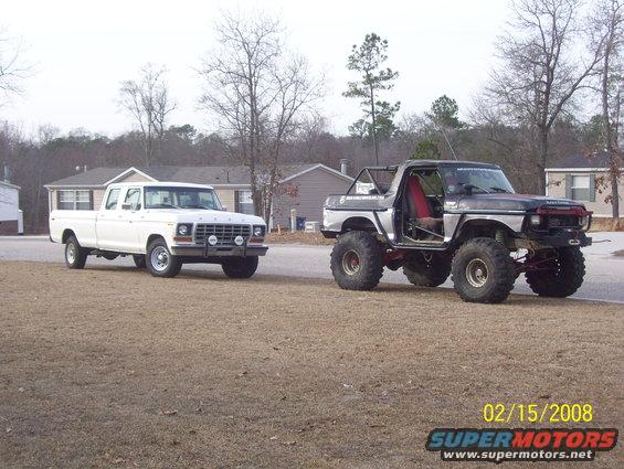 Two Ford trucks, one white crew cab and one lifted silver Bronco, parked on a dirt road