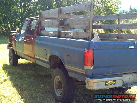 Pickup truck with mismatched doors and wooden bed rails. Has a sticker on the bumper