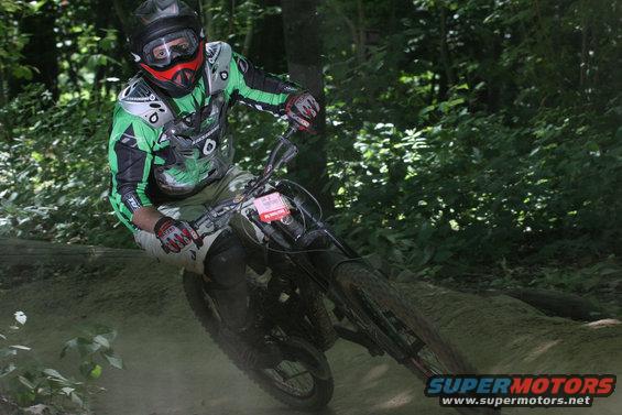 Mountain biker in green and black gear riding a bike on a dirt trail through trees