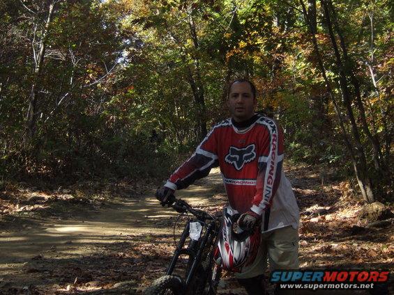 Man in Fox Racing gear with dirt bike in wooded area