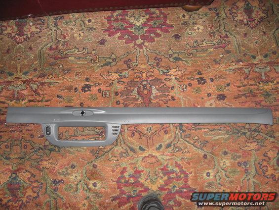 Gray dashboard trim piece with a large cutout and a small circular opening
