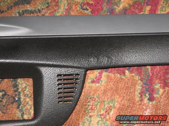Close-up of a black plastic dashboard trim piece with a vent, resting on a patterned carpet