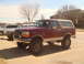 1992 Ford Bronco - A maroon and tan Ford Bronco is parked in a lot with other vehicles visible in the background.