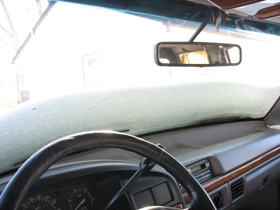 Interior view of a vehicle dashboard with a steering wheel and a rearview mirror. The windshield is covered in frost