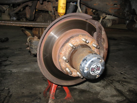 Front wheel hub and brake assembly on red jack stand. Visible is a rusty brake rotor, lug nuts, and a hub cap with "4x4 Automatic" text
