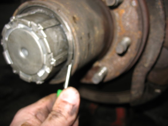 Close-up of a manual locking hub on a vehicle's front wheel assembly. A green-handled tool is being used to adjust a ring