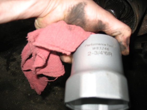 Greasy hand holding a red rag and a Performance Tool socket wrench labeled W83246 2-3/4" 6R